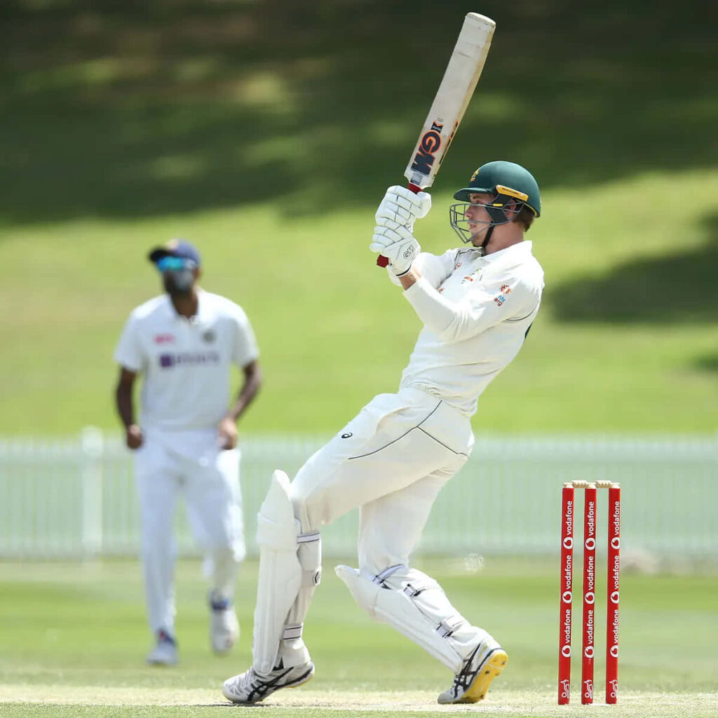 Cameron Green playing cricket in white gear on lush green pitch during live intense match action Wallpaper
