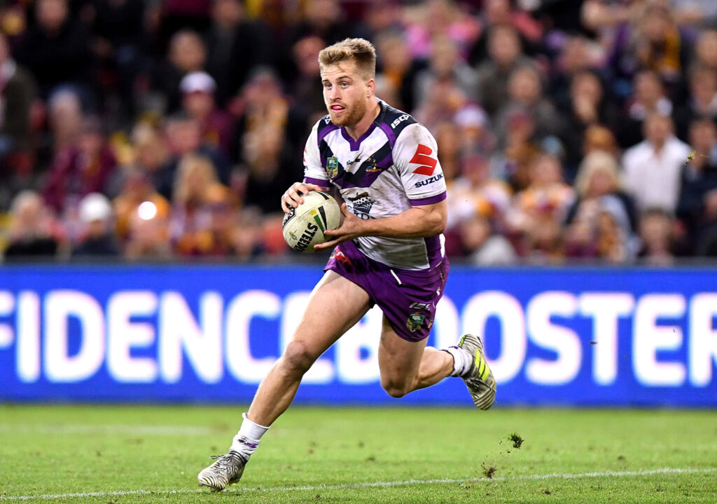 Cameron Munster sprinting with ball in Melbourne Storm purple jersey during intense rugby match Wallpaper