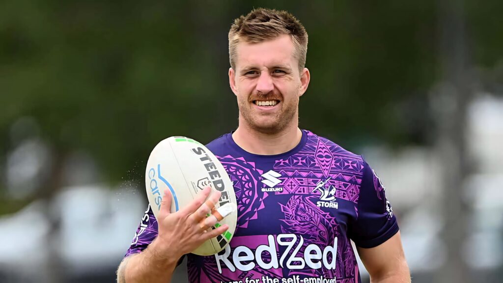 Cameron Munster in purple Melbourne Storm jersey holding rugby ball with confident smile outdoors Wallpaper