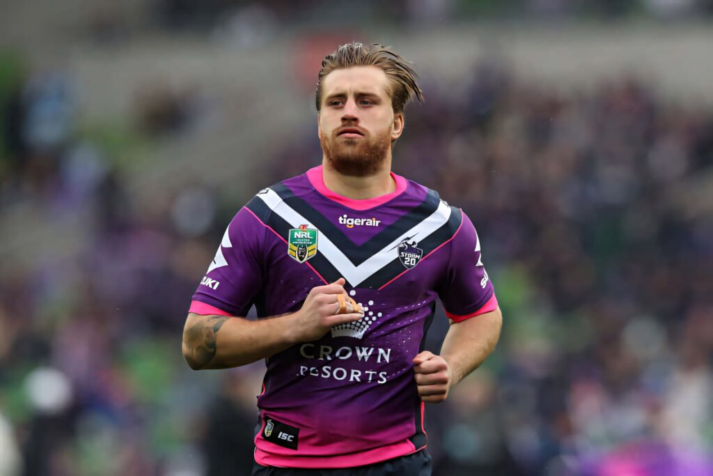 Cameron Munster Melbourne Storm jersey focused expression NRL star blurred stadium background Wallpaper