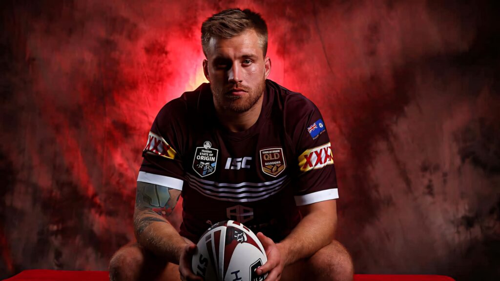 Cameron Munster in Queensland Maroons jersey holding rugby ball with intense focused expression Wallpaper