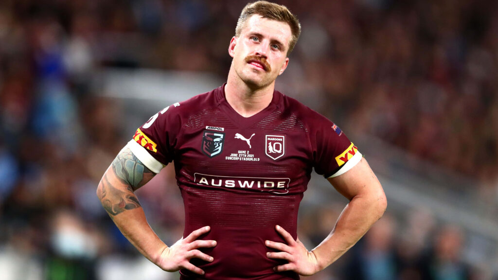 Cameron Munster in maroon Queensland jersey showing determination on field under stadium lights Wallpaper