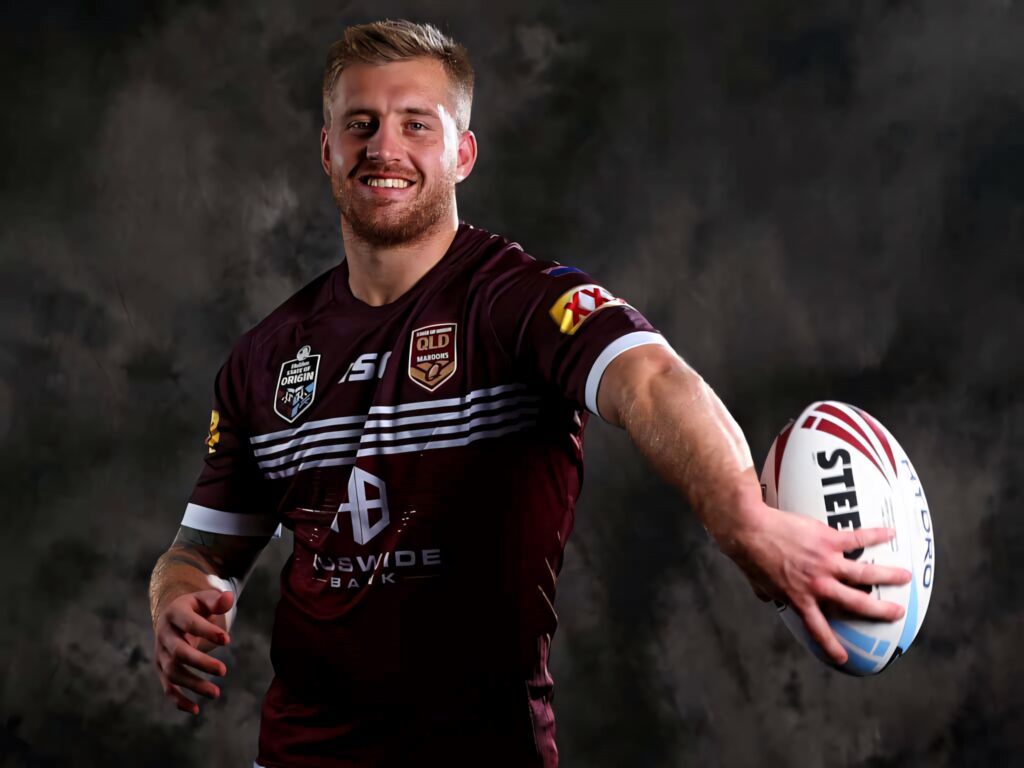 Cameron Munster in maroon Queensland rugby jersey holding Steeden ball dynamic athletic portrait Wallpaper