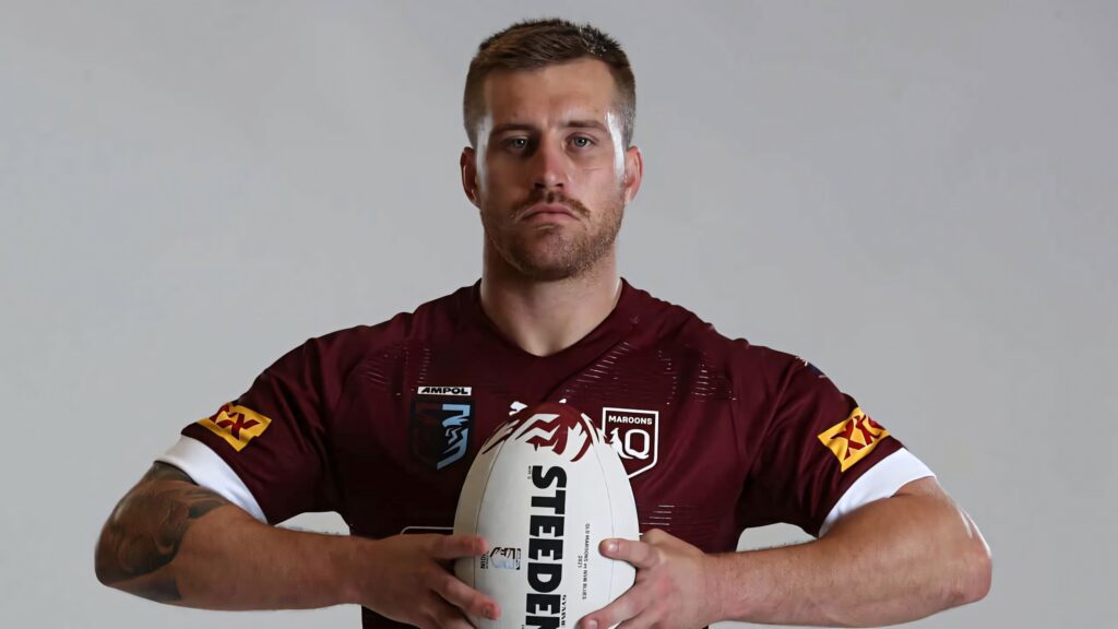 Cameron Munster in maroon Queensland jersey holding Steeden rugby ball focused intense expression Wallpaper