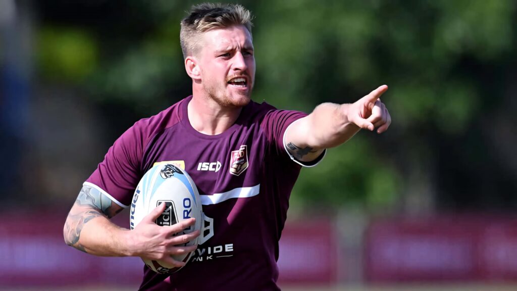 Cameron Munster rugby league star in maroon jersey holding ball intense leadership outdoor background Wallpaper