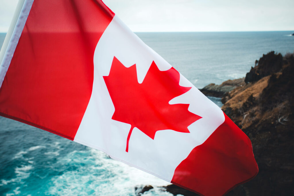 Canadian flag waving with rocky cliffs and blue sea showcasing Canada’s rugged beauty wallpaper