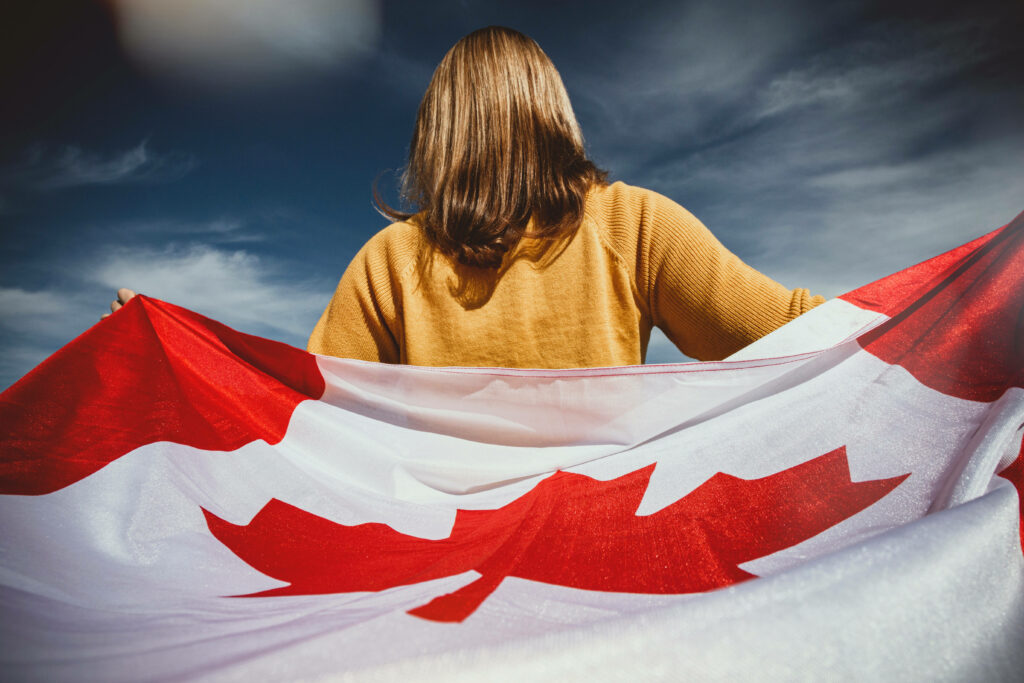Canadian woman in yellow shirt holding red and white flag against dramatic sky background wallpaper
