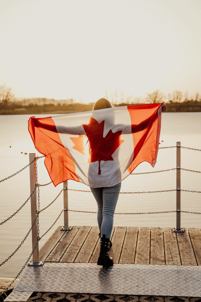 Canadian woman on wooden dock with large Canadian flag in golden sunlight patriotic wallpaper