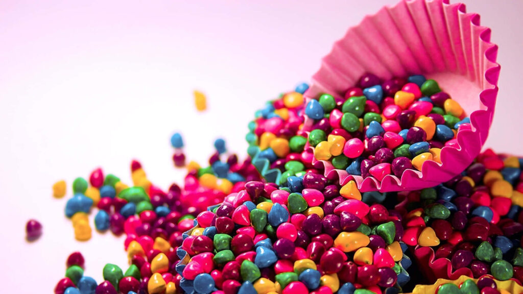 Sugary Delights: Colorful Nerd Candies Spill from a Cupcake Wrapper onto a Scrumptious Desserts Background Wallpaper
