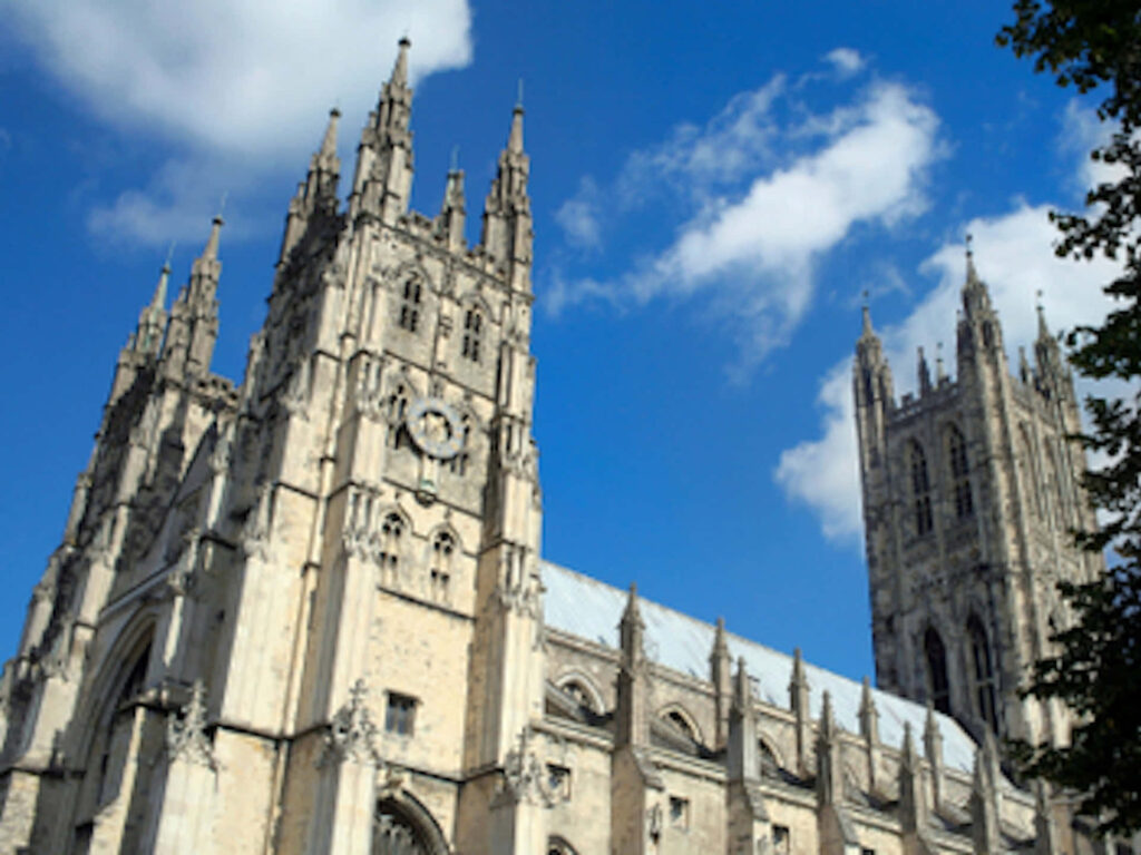Canterbury Cathedral Gothic spires intricate stonework under vivid blue sky with white clouds Wallpaper