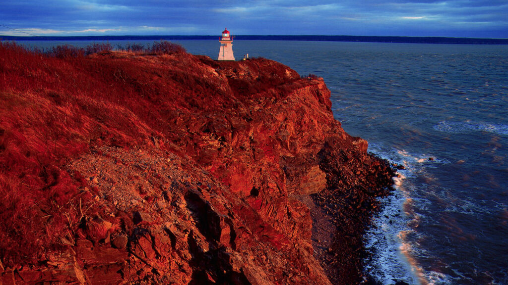 Cape Enrage Canada lighthouse on red sunset cliffside overlooking blue ocean and sky wallpaper