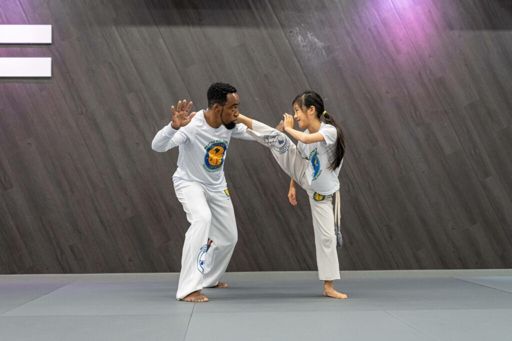 Capoeira coach teaching young student traditional move in modern studio with wallpaper background