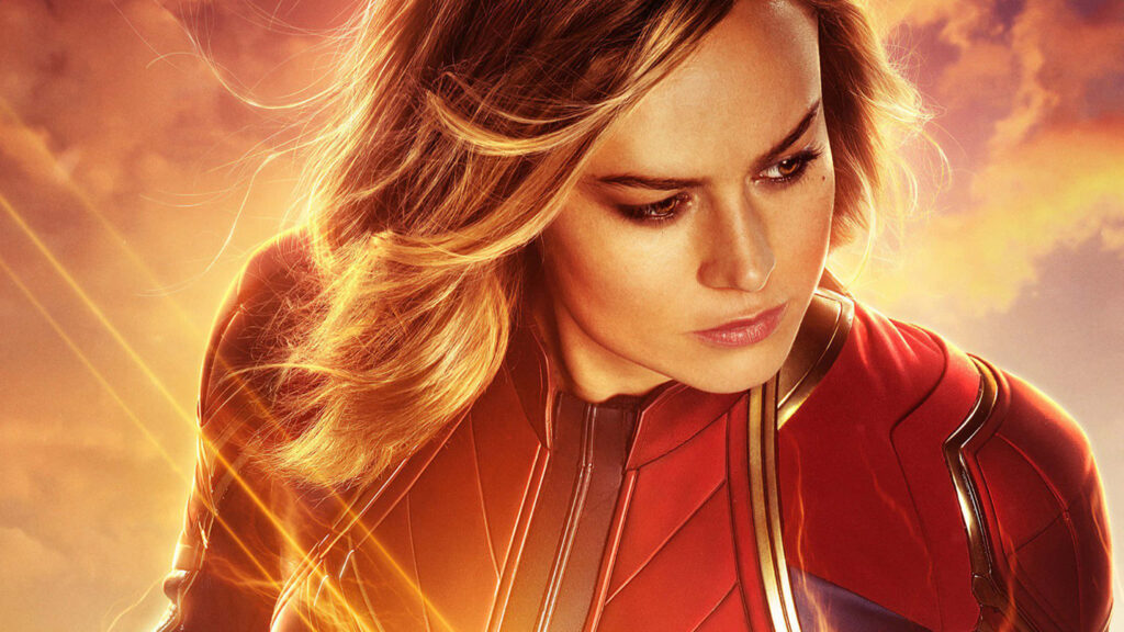 Captain Marvel Brie Larson in red blue gold suit against glowing sky hero Marvel wallpaper background