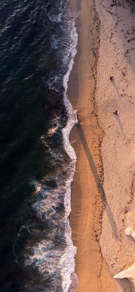 Aerial view of golden hour beach with ocean waves lifeguard tower and long shadows wallpaper