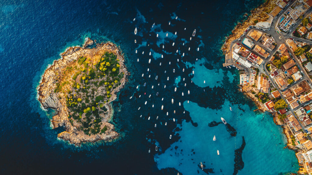 Sail Away to Serene Beauty: A Stunning Aerial View of Pantaleu Island with Sailing Boats, Spain's Nature Oasis - Exquisite 2560x1440 Nature Wallpaper