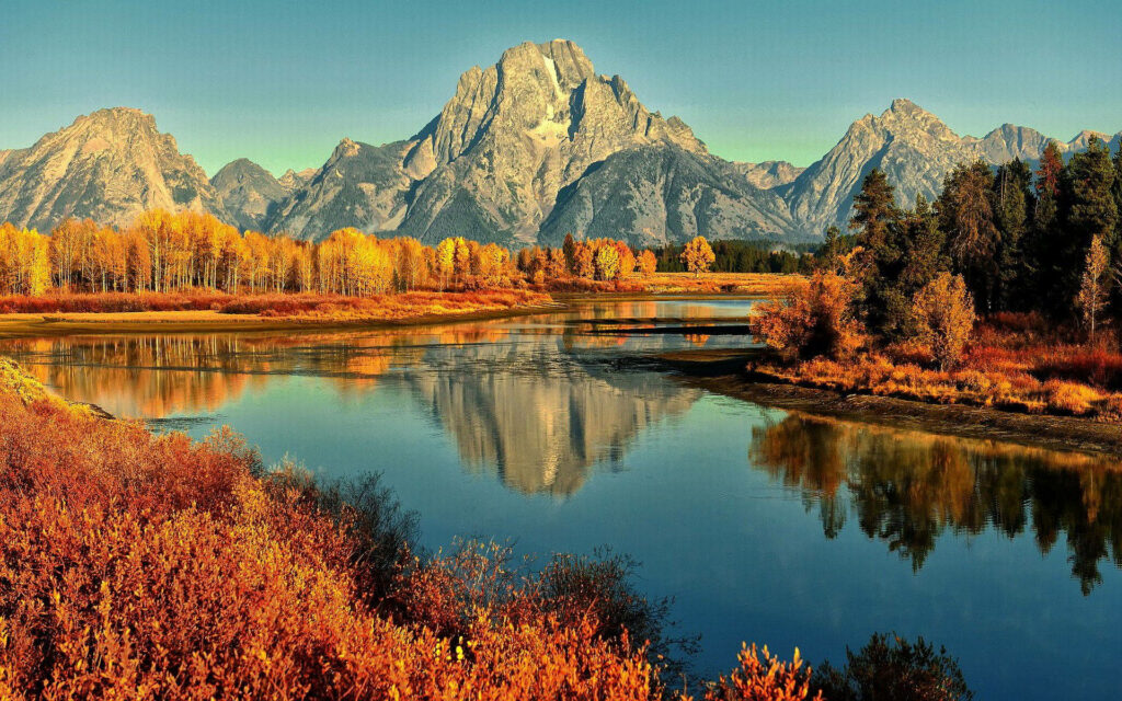 Autumn mountain landscape with vibrant orange and gold foliage reflected in a clear lake Wallpaper