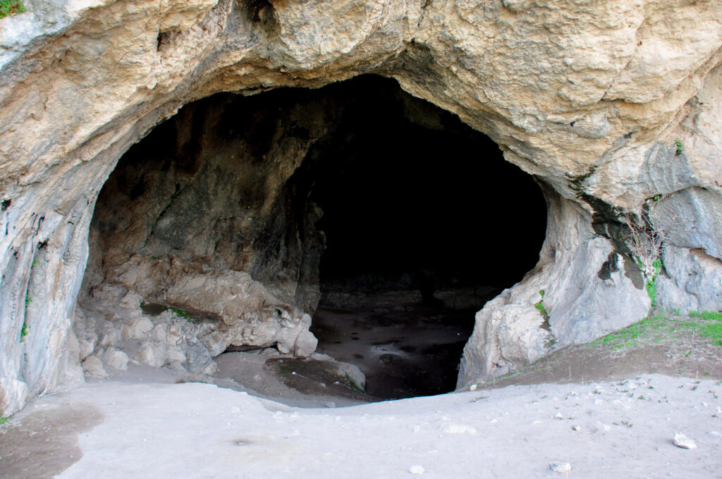 Enchanting Cave Entrance with Sunlit Rock Formations and Earthy Tones Wallpaper