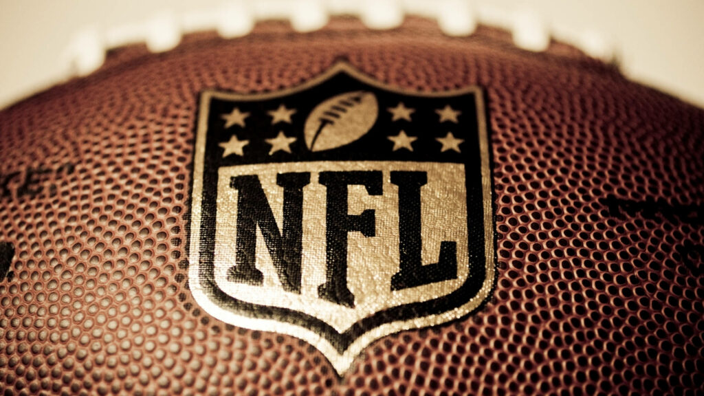 Gridiron Glory: A Captivating Close-Up of NFL Emblem on Football, Blurred Background Enchanting Sports Wallpaper