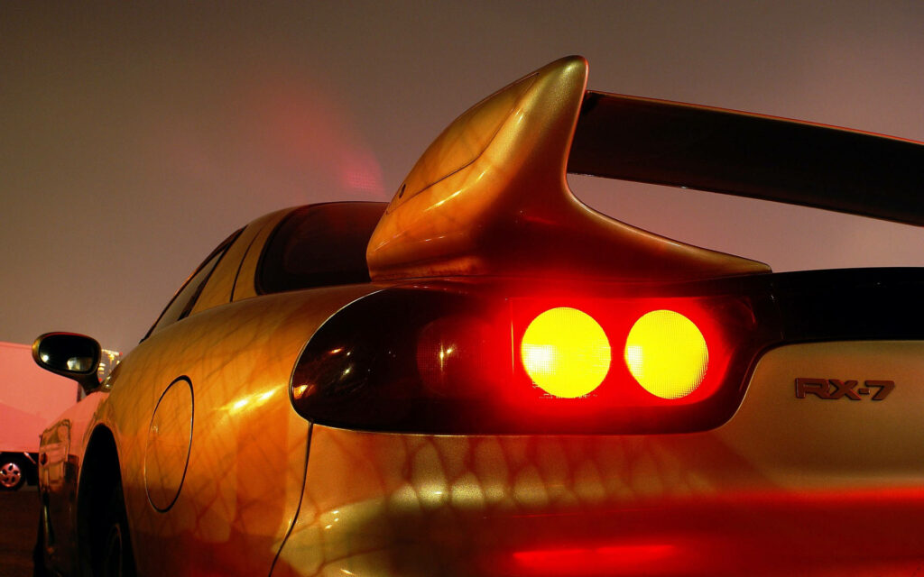 Speed Unleashed: Captivating Close-up of Yellow Mazda RX-7's Tail Light and Rear Wing in Action Wallpaper