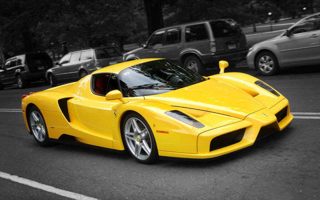 Exquisite Capture of the Top 10 Ferrari Car Models: Vibrant Yellow Ferrari Enzo Poised Against a Dramatic Greyscale Backdrop Wallpaper