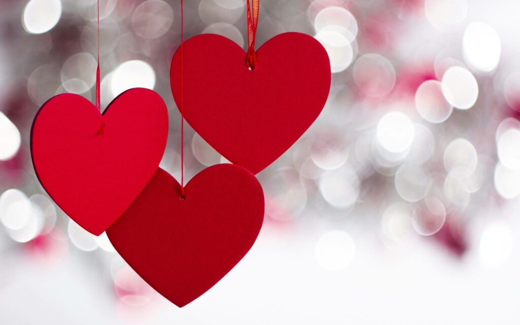 Whimsical Love: Festive Valentine's Day Decor with Red Paper Hearts on Blurred White Background Wallpaper