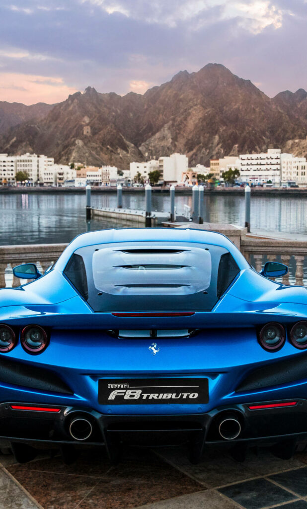 Blazing Through Urban Vistas: Capturing the Majestic F8 Tributo Ferrari amidst Architectural Grandeur and Mountainous Majesty Wallpaper
