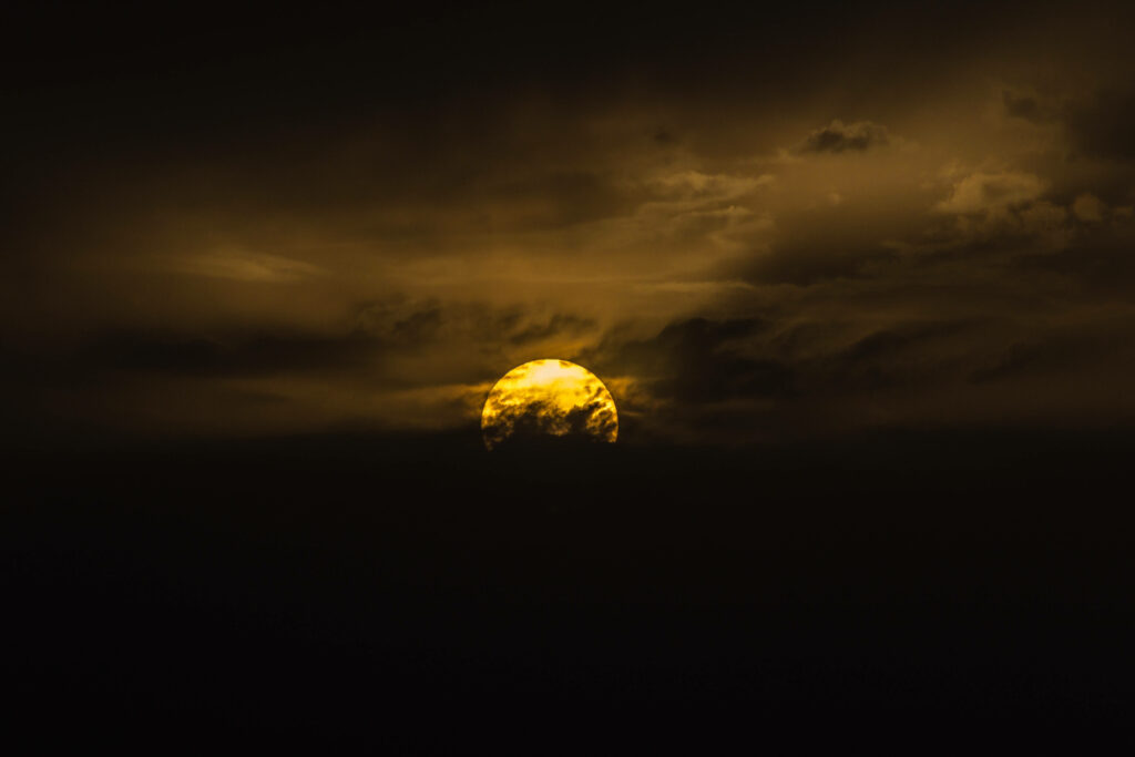 “Moody Wallpaper: Glowing Yellow Sun Behind Dramatic Clouds”