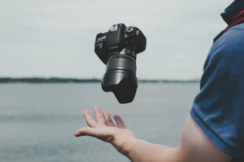 Surreal black Canon DSLR camera floating above hand on desaturated waterfront wallpaper background