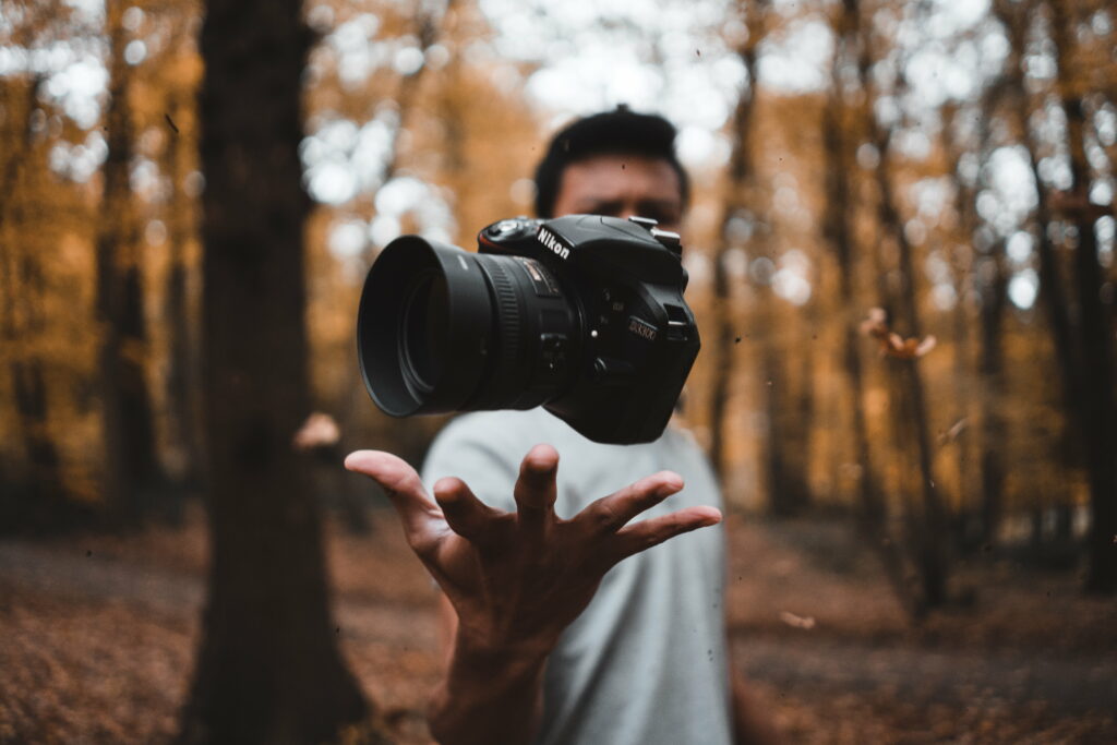 Capturing the Wilderness: Black DSLR Camera Floats in Man's Hand Against Woodland Wallpaper