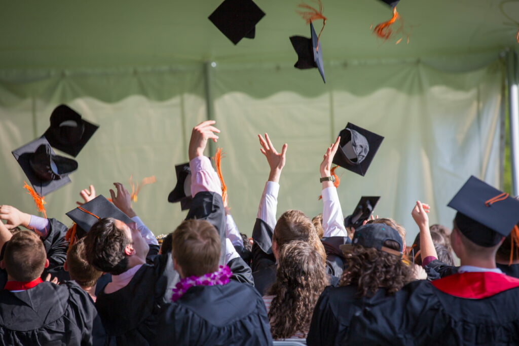 Group of graduates in black gowns tossing caps celebrating academic success wallpaper background