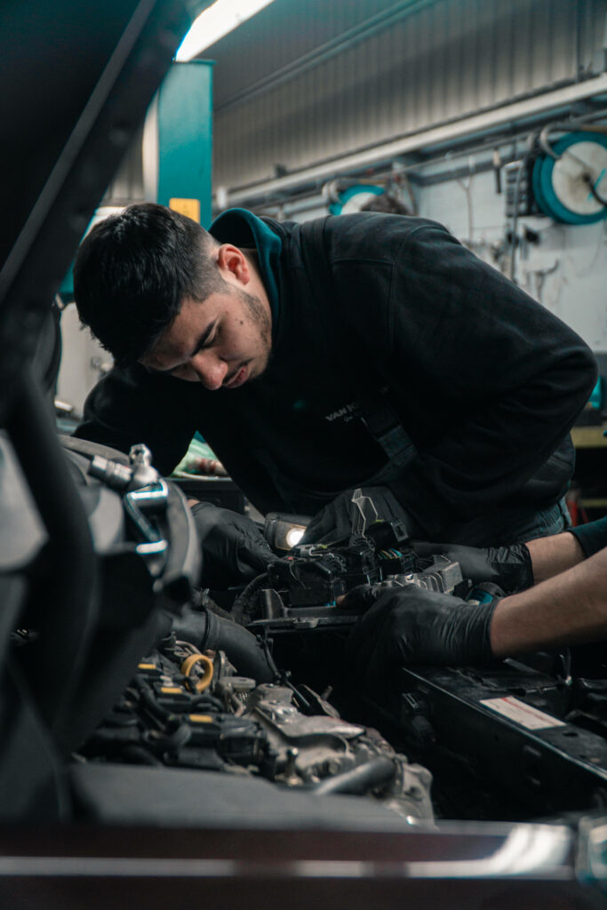 Car mechanic wearing gloves inspecting vehicle engine in workshop with tools and machinery Wallpaper