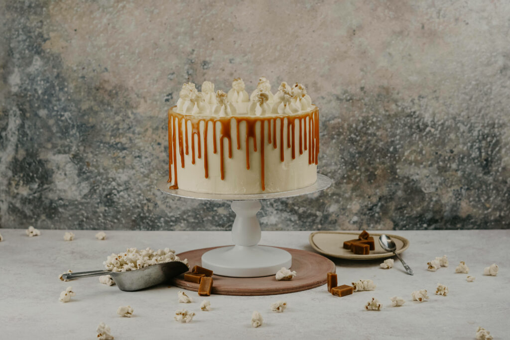 Caramel popcorn cake with white frosting and caramel drip on pedestal with scattered popcorn Wallpaper