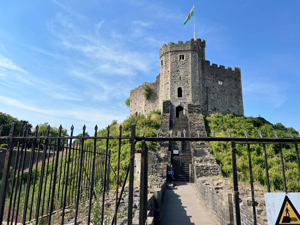 Cardiff Castle gate stone tower with Welsh flag bright blue sky lush greenery medieval path Wallpaper