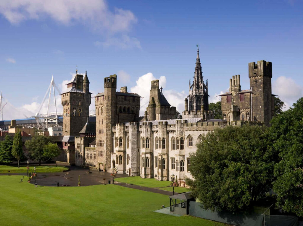 Cardiff Castle with Gothic towers and stone walls under blue sky surrounded by green lawns Wallpaper