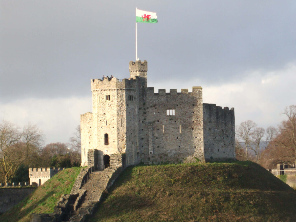 Cardiff Castle on grassy mound with stone walls and Welsh flag under clear blue sky wallpaper background