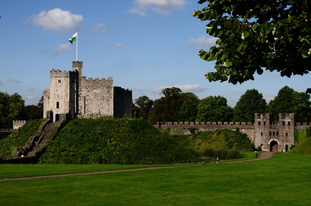 Cardiff Castle with medieval stone walls and flag under blue sky surrounded by green lawns Wallpaper
