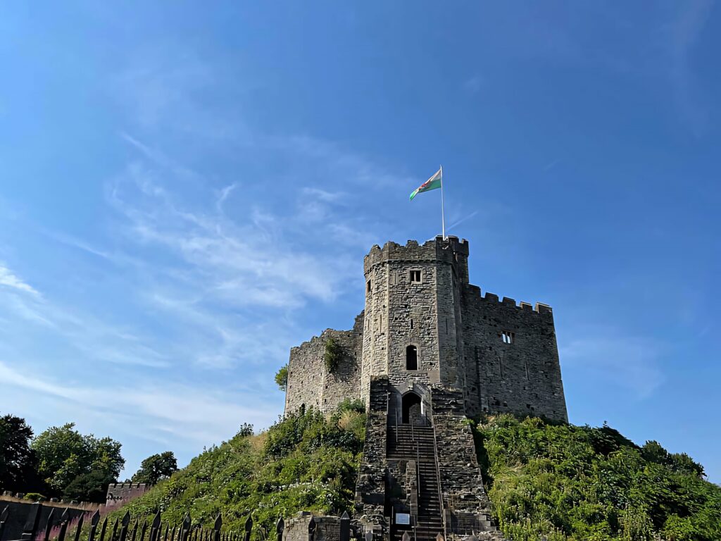 Cardiff Castle stone keep on green hill under blue sky with Welsh flag waving heritage wallpaper