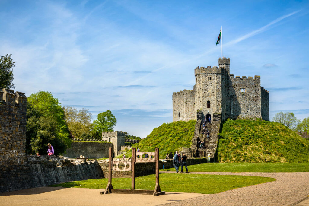 Cardiff Castle stone keep on grassy mound with blue sky lush trees medieval Welsh landmark view Wallpaper
