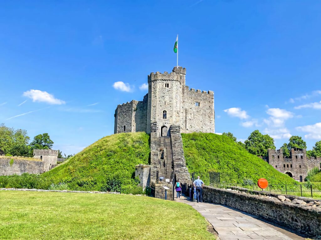 Cardiff Castle with Welsh flag bright blue sky lush green grass historic stone architecture Wallpaper