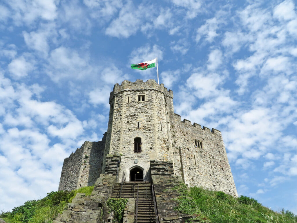 Cardiff Castle historic grey stone walls Welsh flag vibrant sky dramatic clouds background Wallpaper