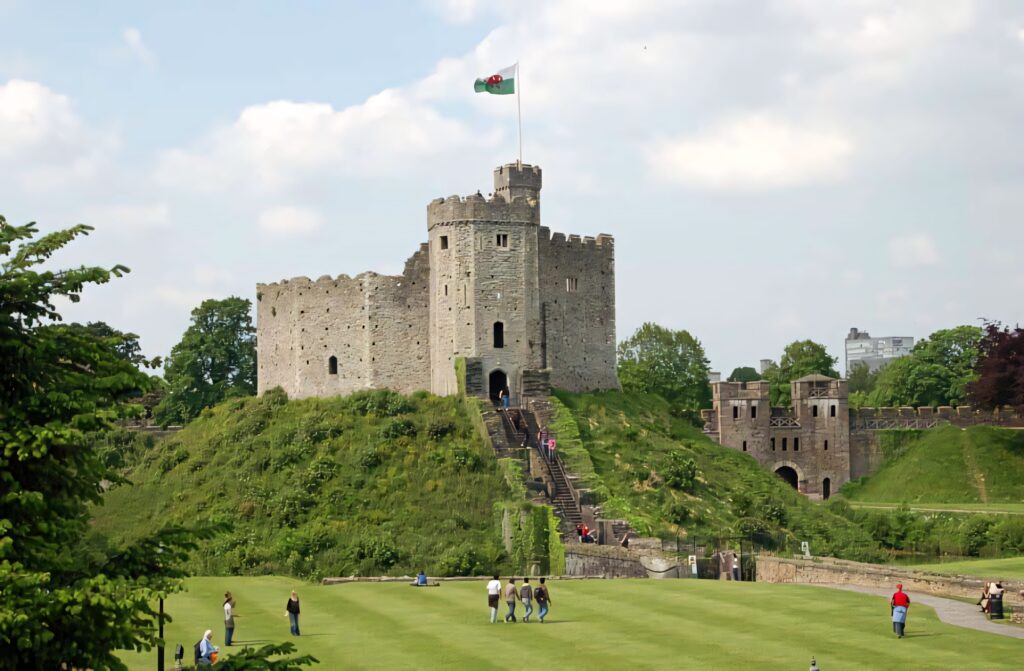 Cardiff Castle historic fortress on green mound with Welsh flag and visitors under blue sky Wallpaper