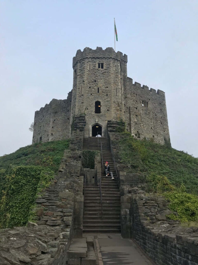 Cardiff Castle stone tower with flag staircase and lush greenery under a cloudy sky wallpaper