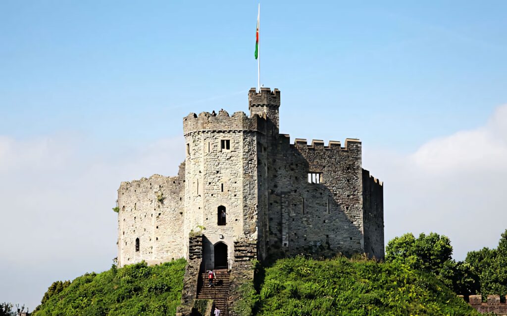 Cardiff Castle medieval stone towers with flag under clear blue sky and lush green trees Wallpaper