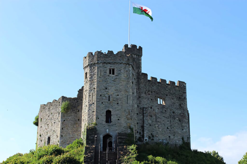Cardiff Castle medieval stone tower with Welsh flag under blue sky surrounded by green trees wallpaper