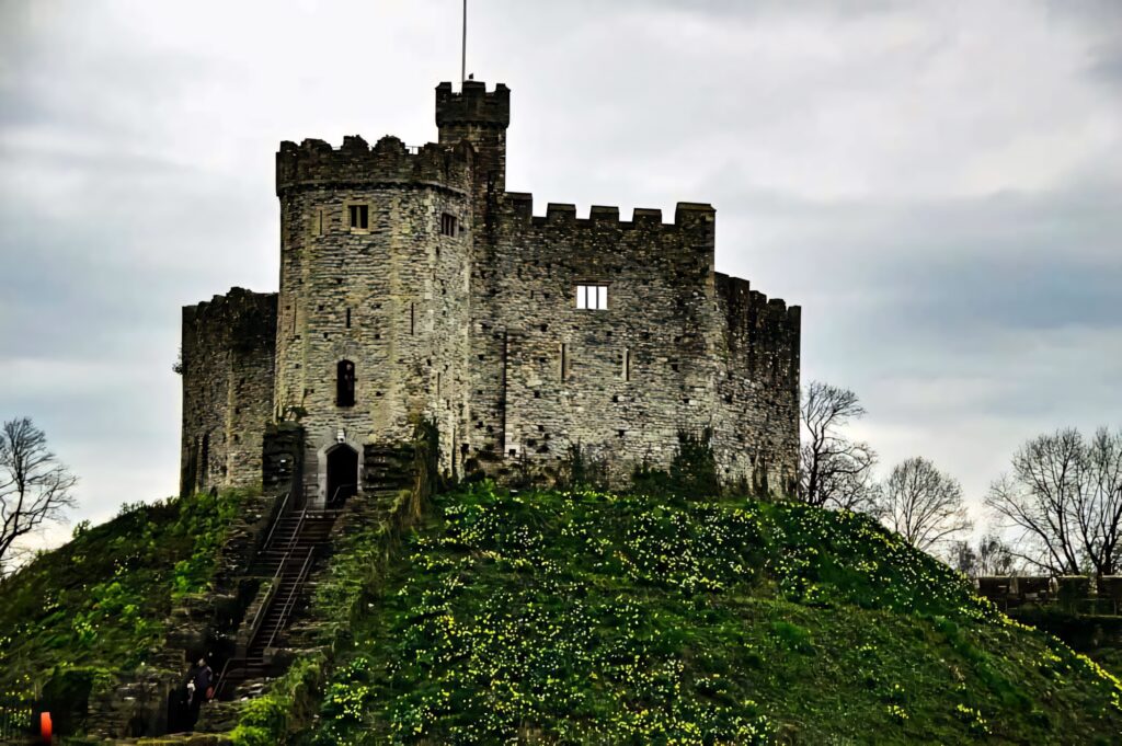 Cardiff Castle on green hill with ancient stone walls under dramatic cloudy sky wallpaper background