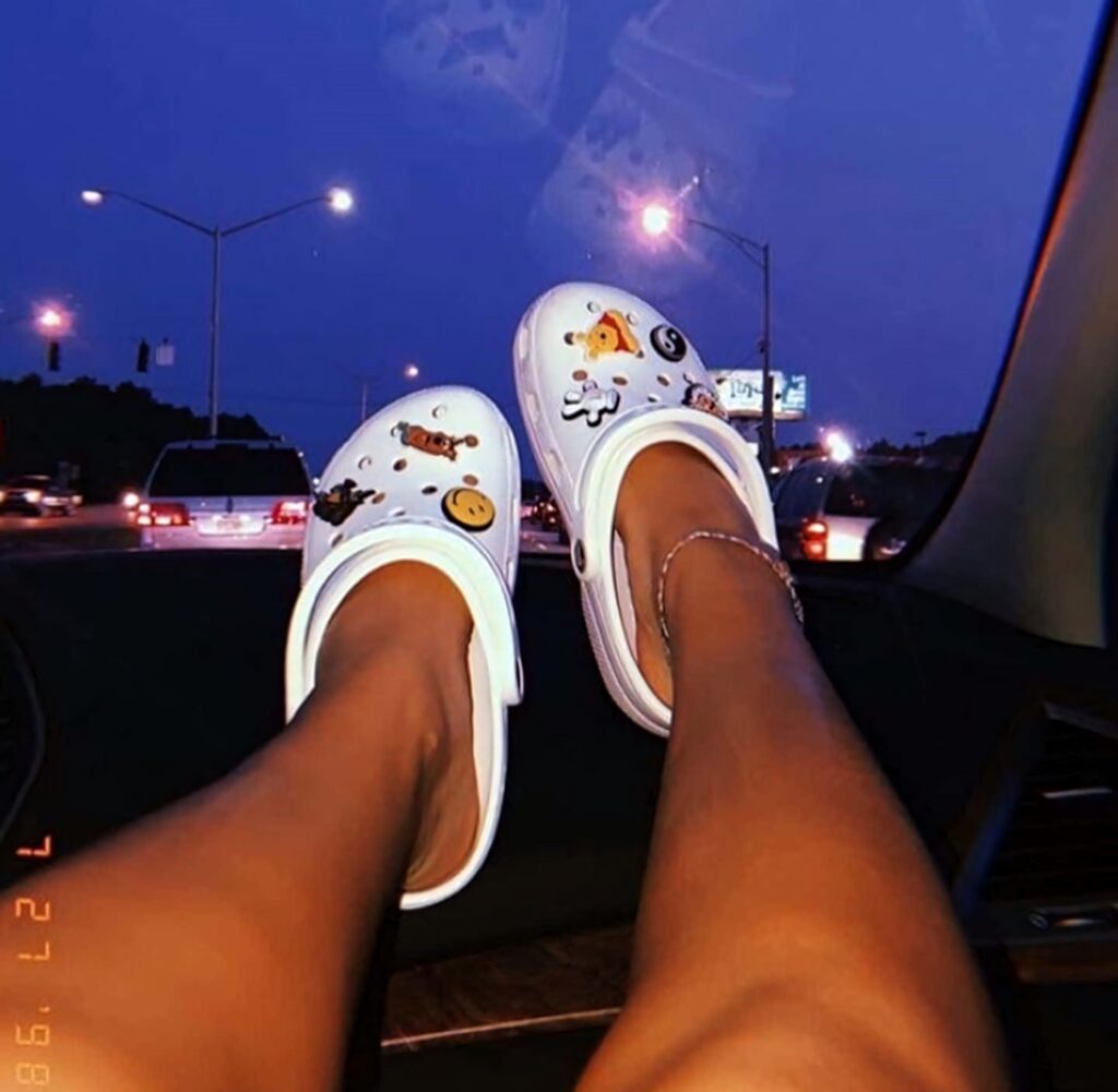 Woman relaxing in car at dusk with colorful cartoon charm white clogs on dashboard city street background Wallpaper