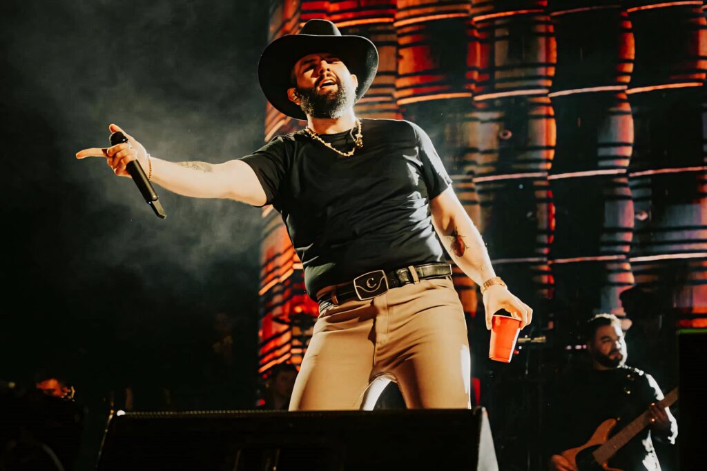 Carin León performing live in cowboy outfit on stage with warm lighting and rustic barrel backdrop Wallpaper