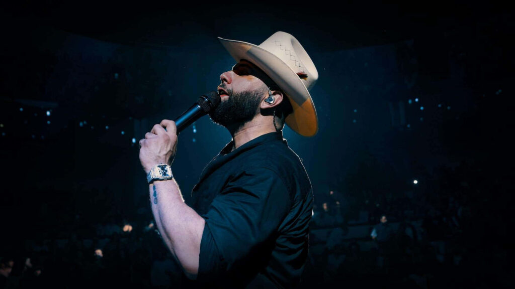 Carin León live country performance with cowboy hat and dramatic stage lighting wallpaper background