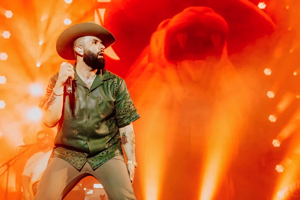 Carin León performing live on stage with warm orange lighting and dramatic concert spotlights Wallpaper