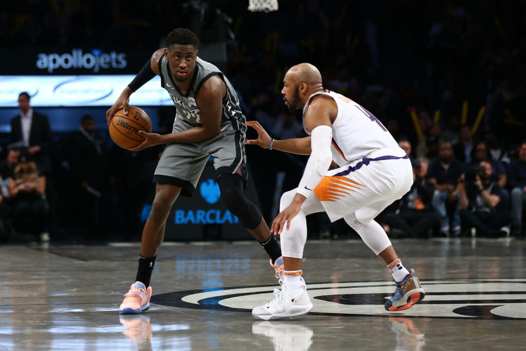 Caris LeVert dribbles past PJ Tucker in intense basketball game with vibrant arena lighting Wallpaper